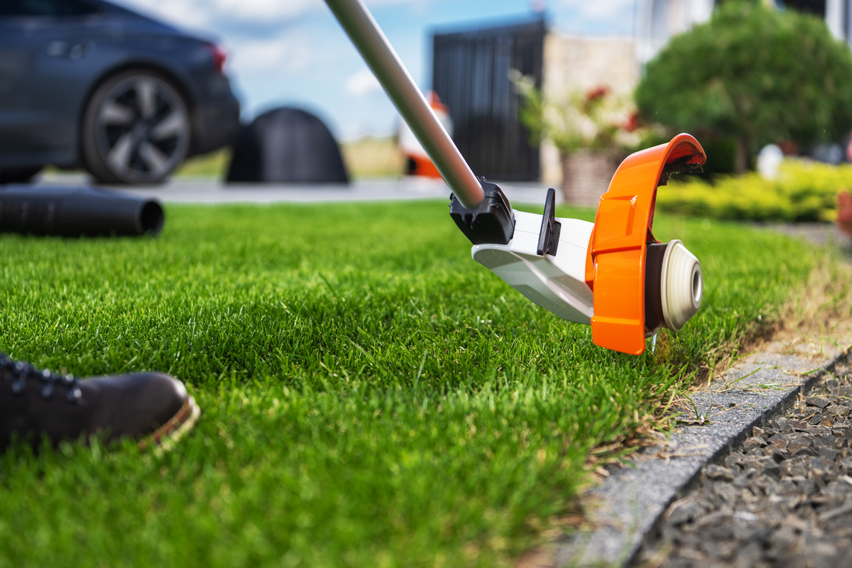 Trimming Lush Green Grass Along a Driveway With a Weed Eater on a Sunny Day in a Suburban Garden